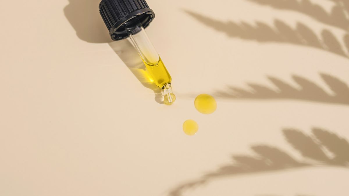 CBD oil dropper with golden drops on a beige surface