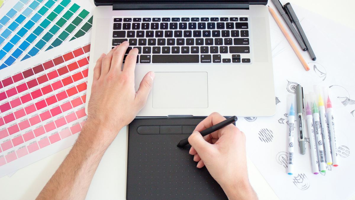Designer sketching on a drawing tablet beside colour swatches